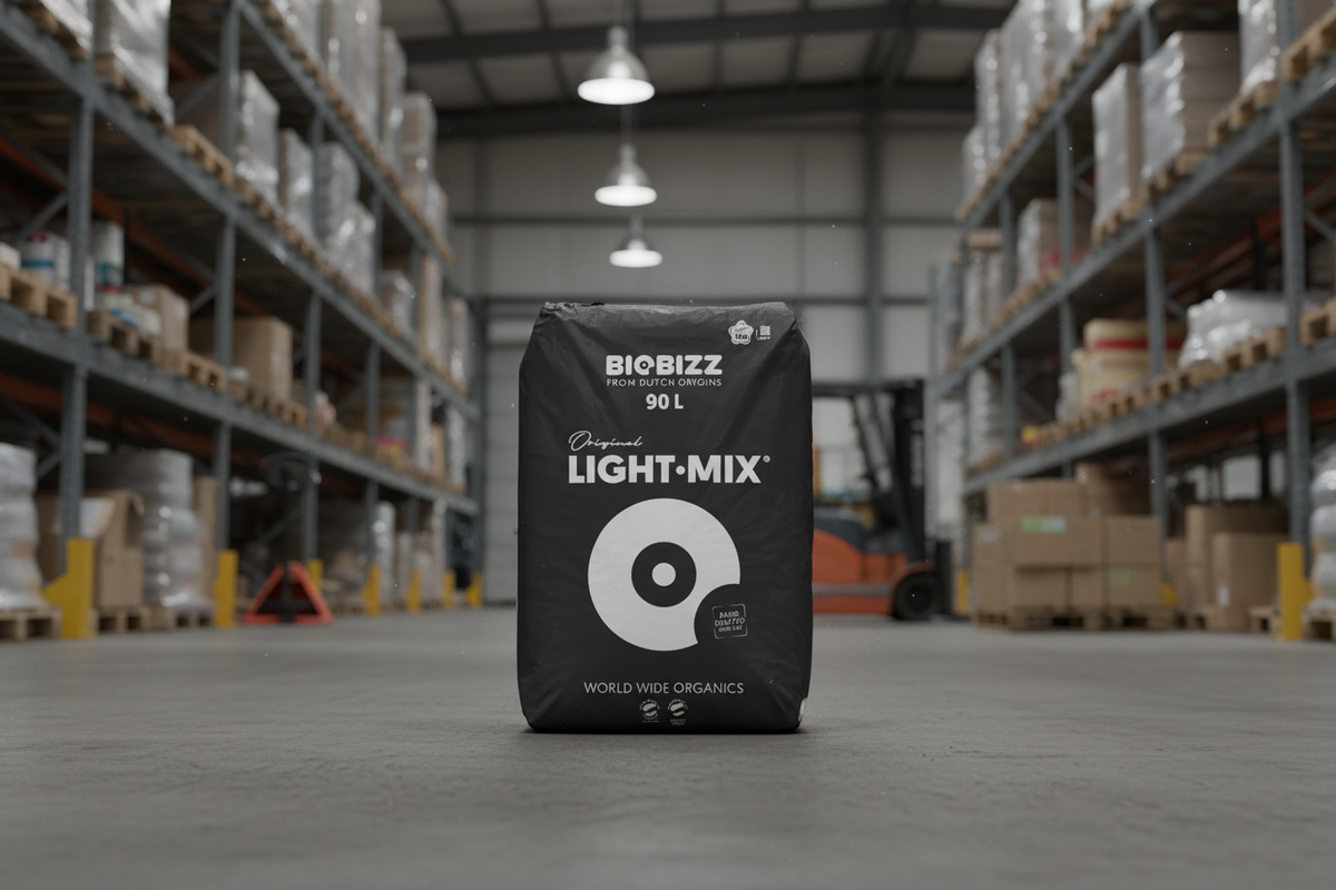 A black bag of BioBizz 90L Classic Light-Mix organic compost positioned in the center of a warehouse aisle, with shelving and pallets blurred in the background.