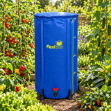 A blue FlexiGrow flexible rain barrel cover with yellow branding and measurement markings, shown in a lush garden setting with tomato and cucumber plants.