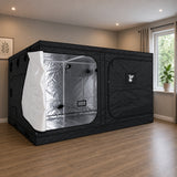 A large black GorillaBox Deluxe grow tent measuring 4m-3m-2m with a reflective silver interior, set up in a home room with wood floors and a window.