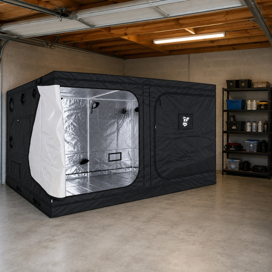 A black GorillaBox Deluxe grow tent measuring 4m-3m-2m with a reflective silver interior and side opening, set up inside a concrete garage with shelving and tools visible in the background.