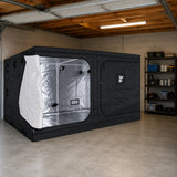 A black GorillaBox Deluxe grow tent measuring 4m-3m-2m with a reflective silver interior and side opening, set up inside a concrete garage with shelving and tools visible in the background.