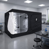 A black GorillaBox Deluxe grow tent measuring 4m-3m-2m with a reflective silver interior and a white front flap, set up in a clean laboratory or studio space with tables, cabinets, and equipment visible.