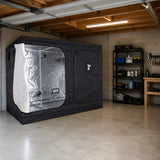 A black GorillaBox Deluxe grow tent measuring 5m-4m-2.2m with a reflective silver interior and side opening, set up inside a concrete garage with shelving and tools visible in the background.