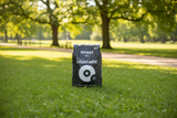 A black bag of BIOBIZZ Light-Mix 90L lawn fertilizer stands on a green grassy lawn in a sunny park with blurred trees in the background.