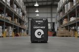 A black bag of BioBizz 90L Classic Light-Mix organic compost positioned in the center of a warehouse aisle, with shelving and pallets blurred in the background.