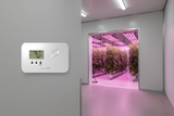 hvacLINK control panel with digital display  on wall next grow room with plants and lights.