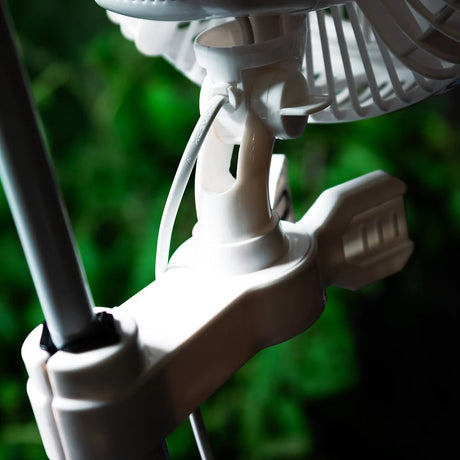 Close-up of a white plastic fan mount with a mounting pole and part of a fan blade, set against a blurred green background.