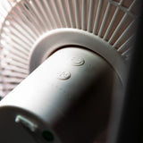 A close-up shot of a white cylindrical fan motor housing, with ribbed detailing and small circular buttons on the top surface.