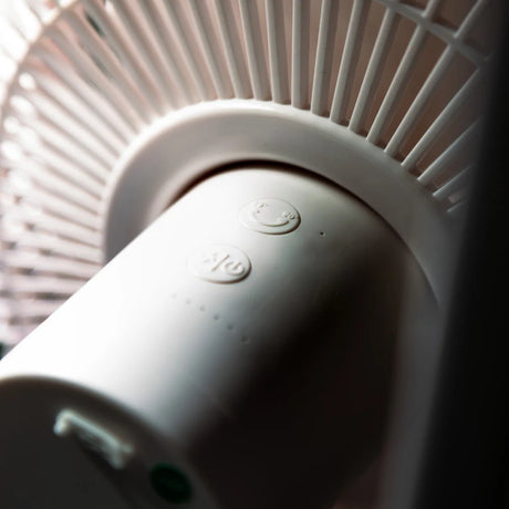 A close-up shot of a white cylindrical fan motor housing, with ribbed detailing and small circular buttons on the top surface.