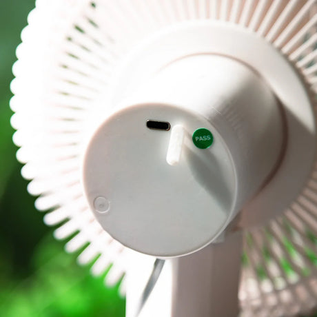 Close-up of a white fan showing the back of the motor housing with a USB-C port and a green PASS switch, set against a blurred green background.